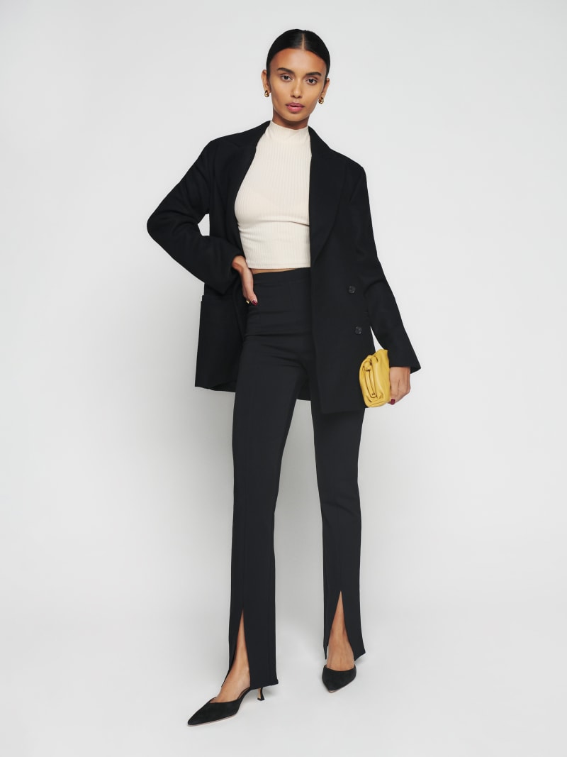 A woman wearing black Petites Fletcher Pants with a high waist, slim fit, straight cut, and a small slit at the bottom of each pant leg.
