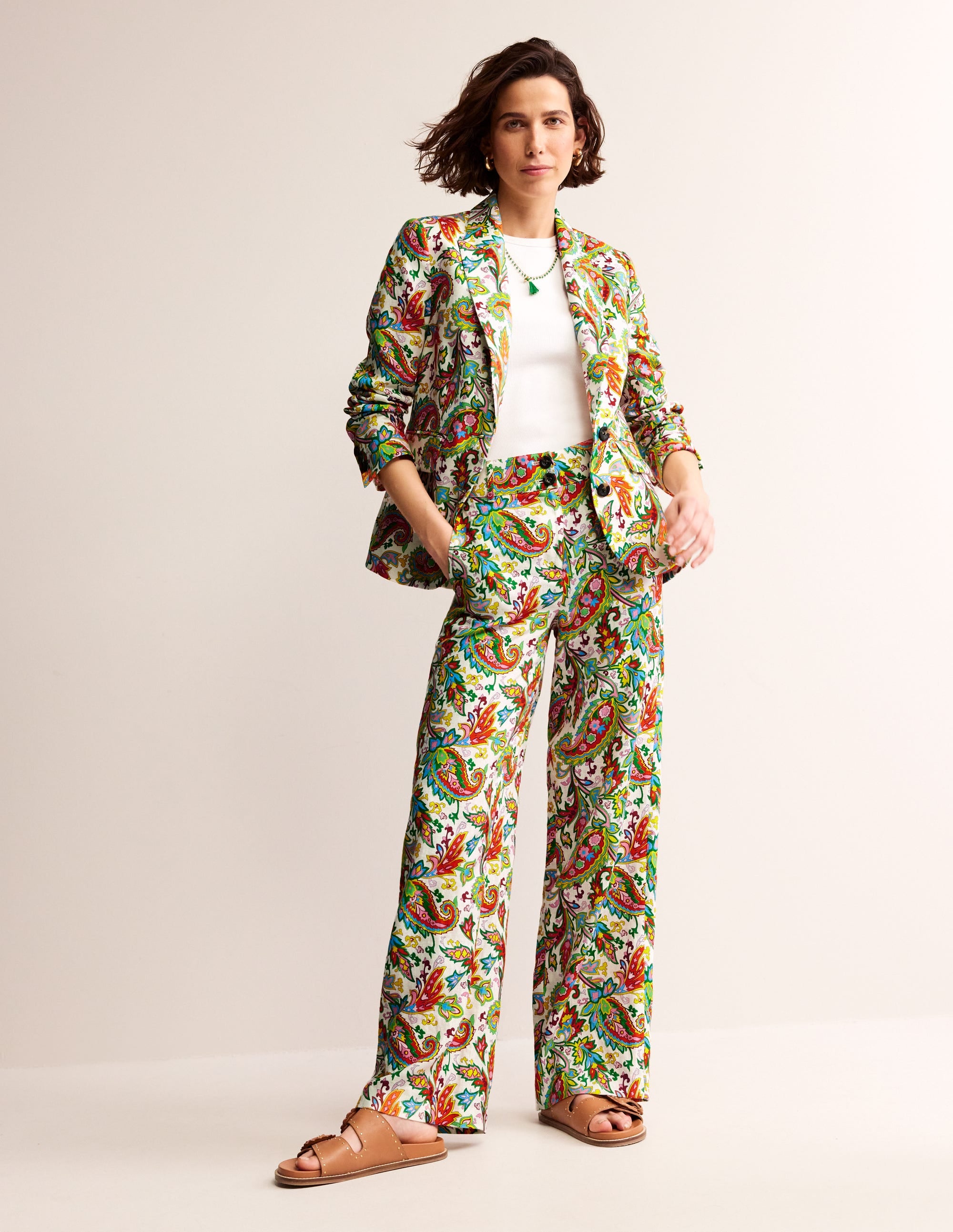 A woman wearing ivory wide-leg linen trousers with a blue paisley pattern, paired with a matching blazer, white top, and tan sandals.
