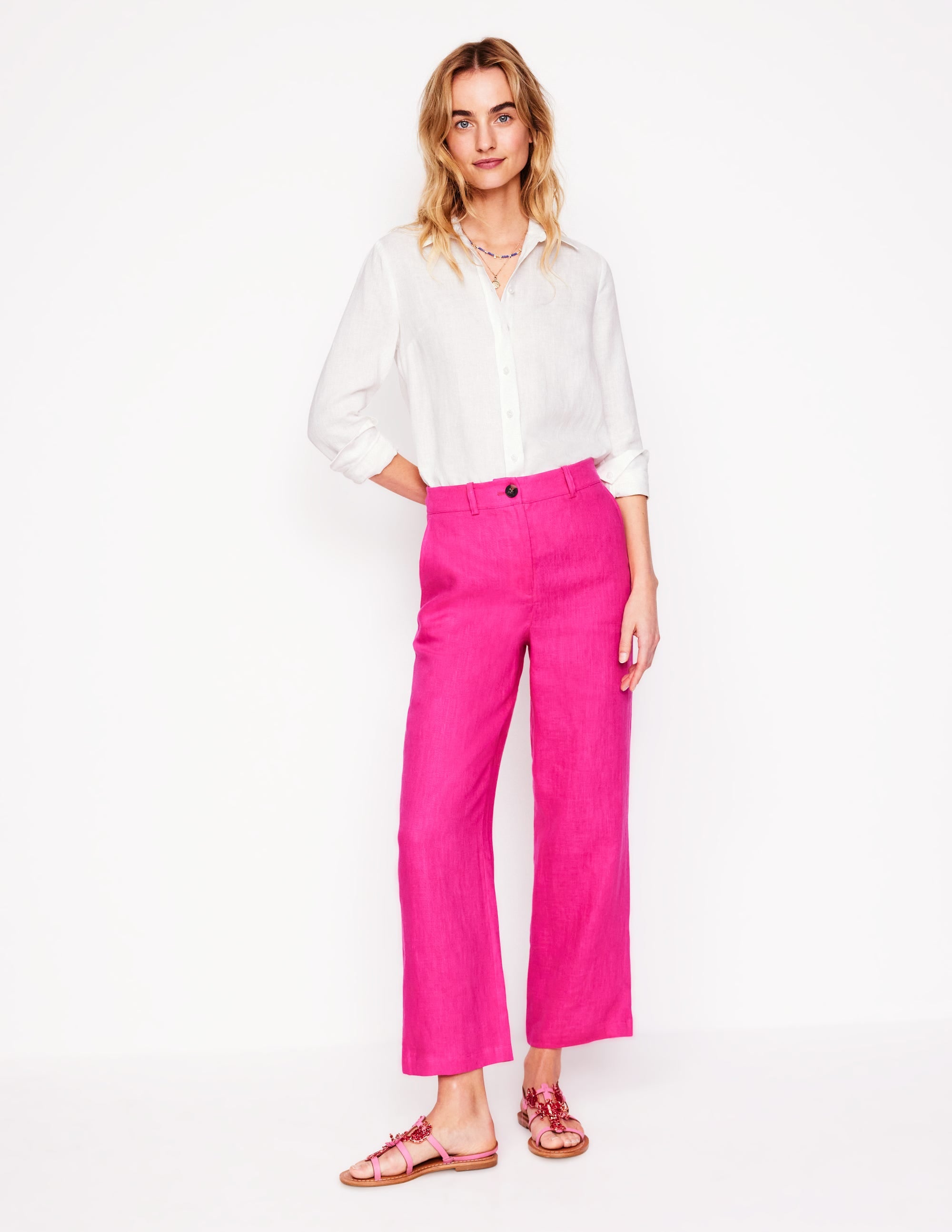 A woman wearing bright pink wide-leg cropped linen trousers with a white shirt, standing against a plain background.
