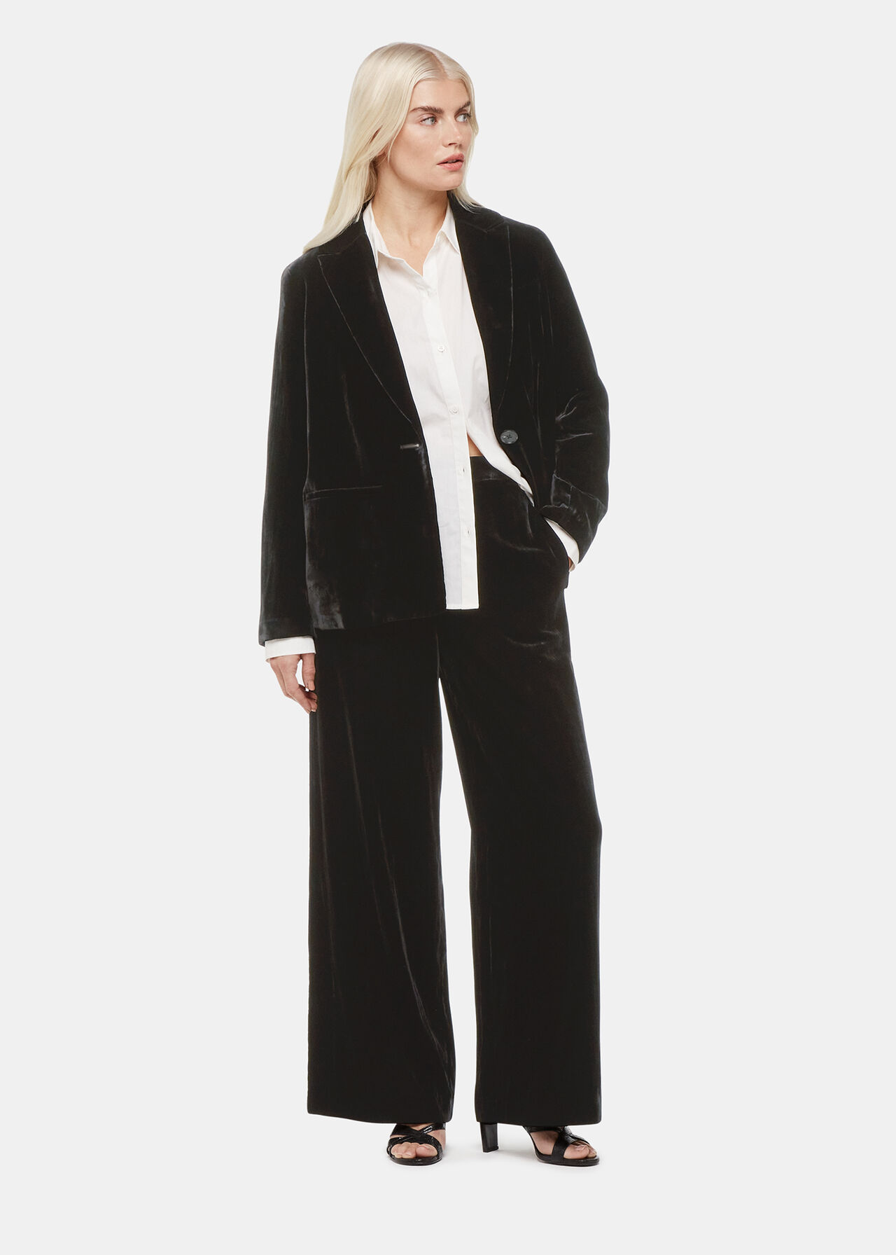 A woman wearing a black velvet blazer with a white shirt underneath, paired with black wide-leg trousers and black heels.