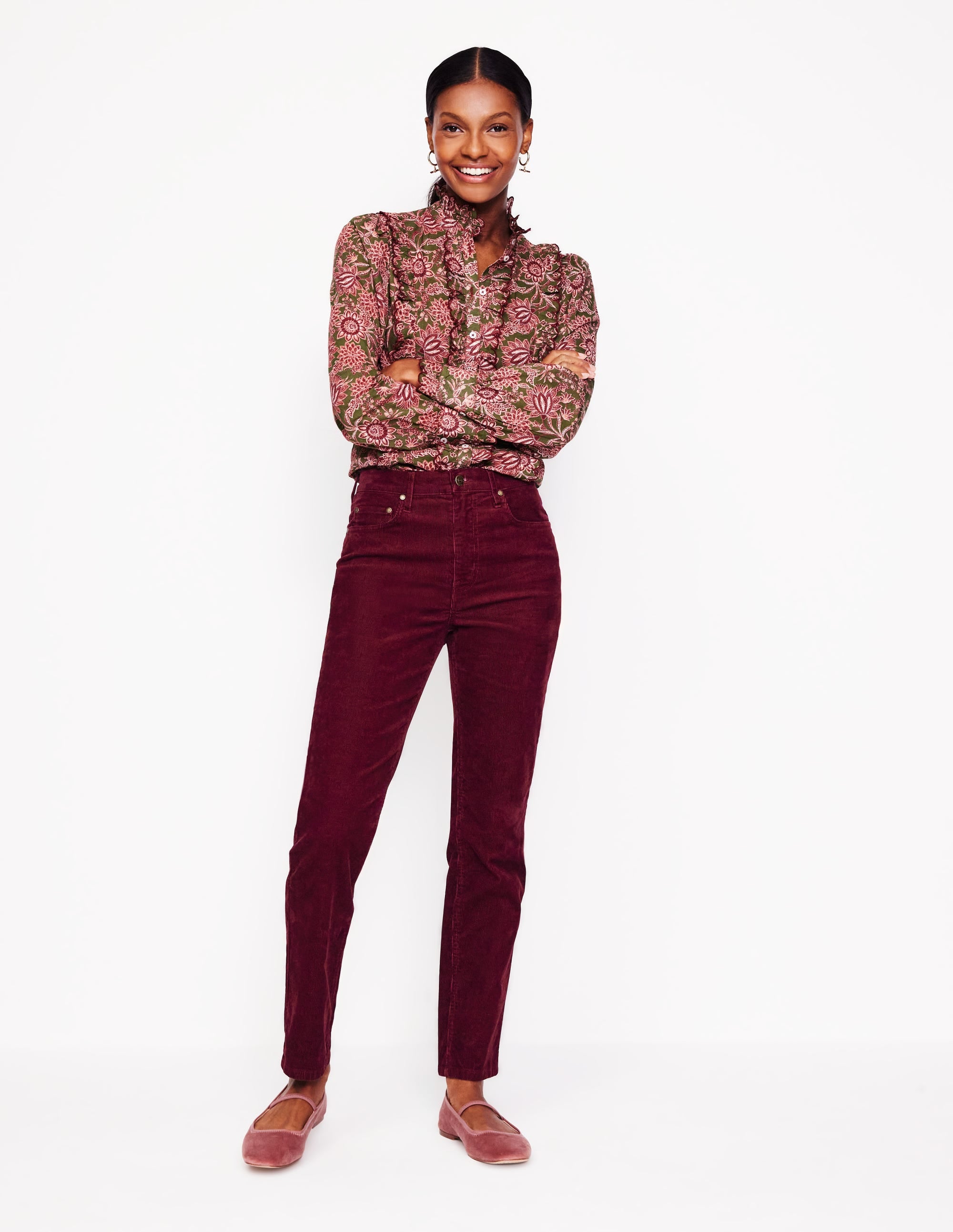 A woman wearing deep wisteria colored corduroy jeans with five pockets, a button at the waist, and a zipped fly, paired with a floral blouse.