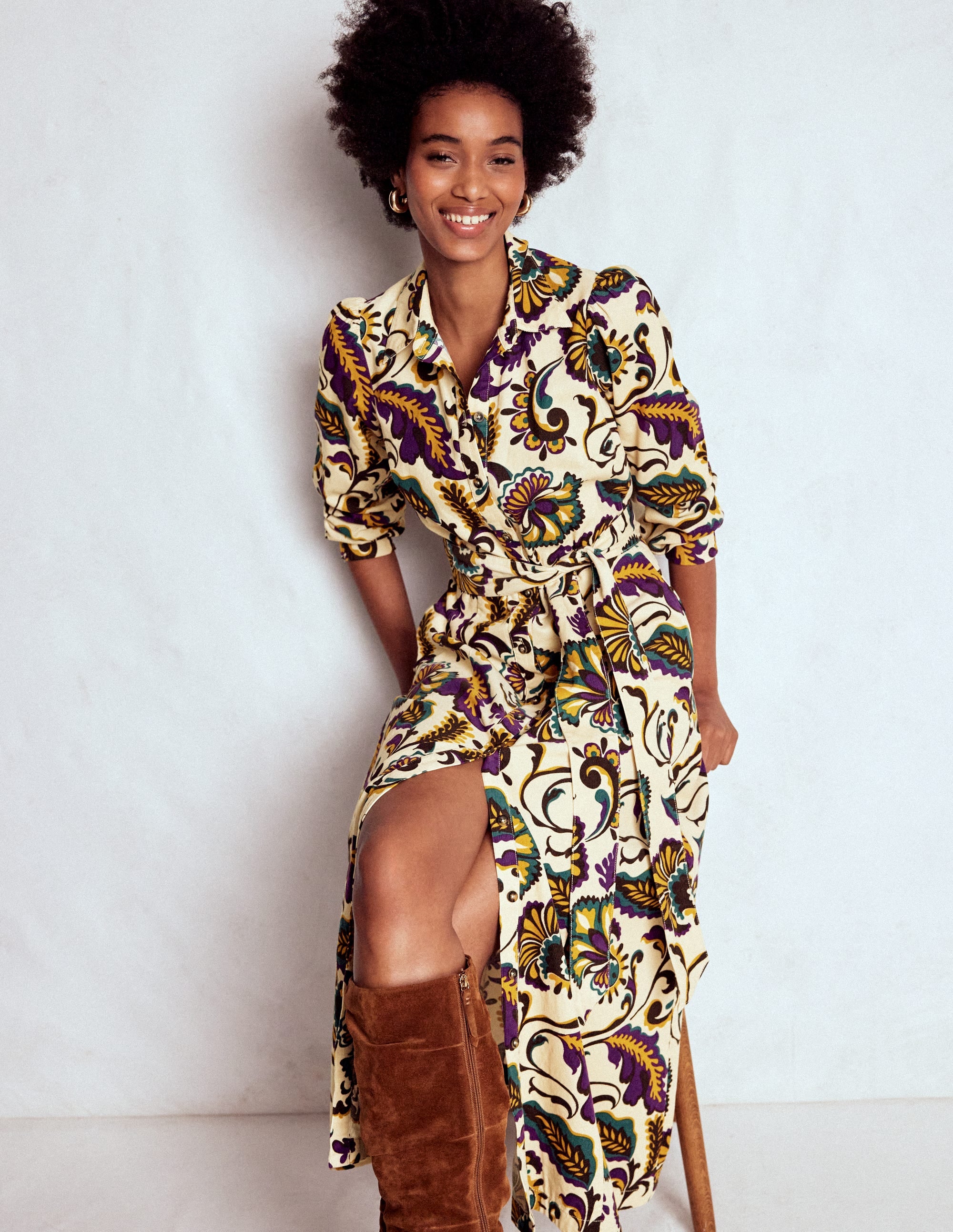A woman wearing a colorful, patterned midi dress with statement sleeves, pockets, and a belt, standing against a plain background.