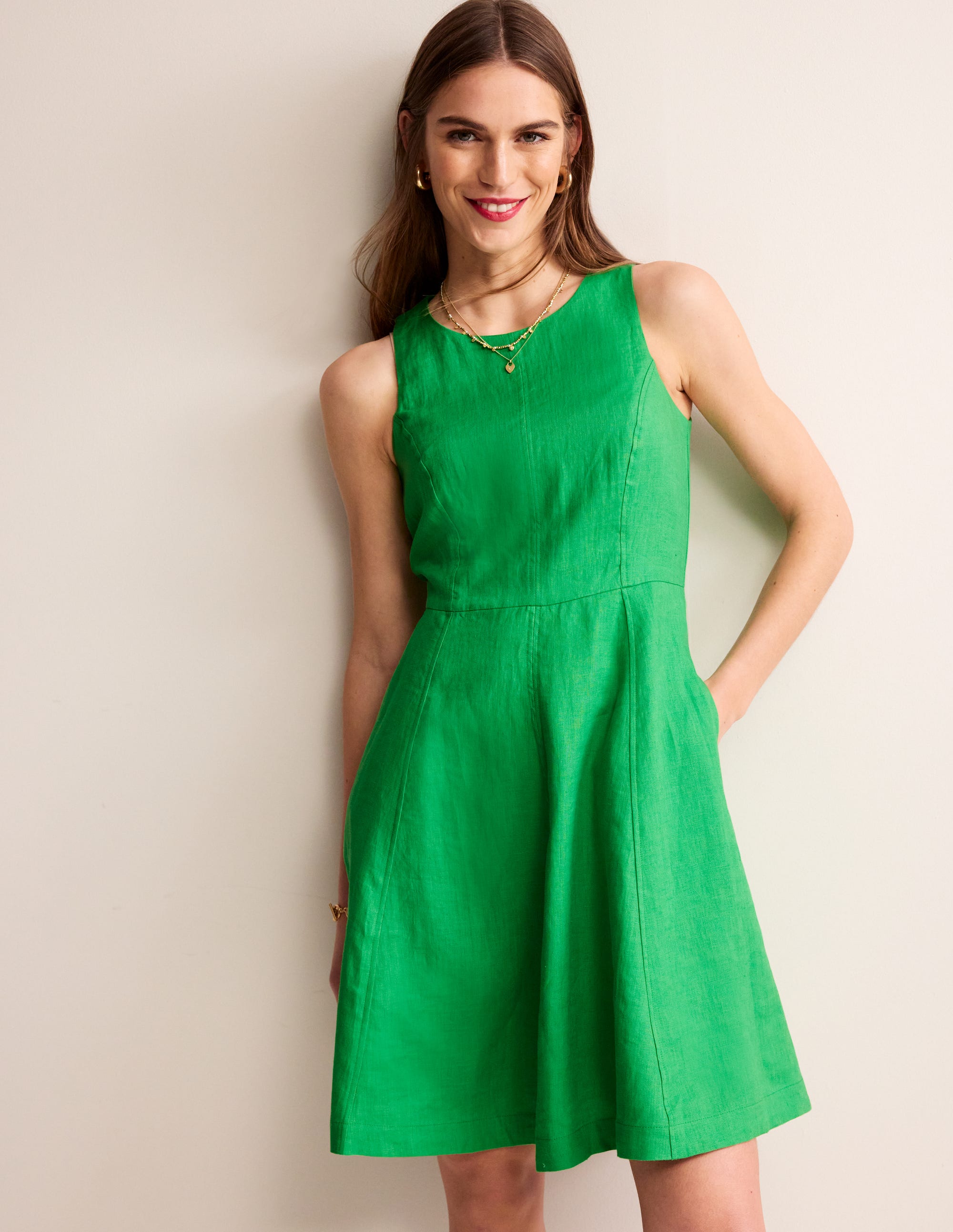 A woman wearing a sleeveless, knee-length Kelly Green linen dress with a flared skirt, lined bodice, and back button detail.