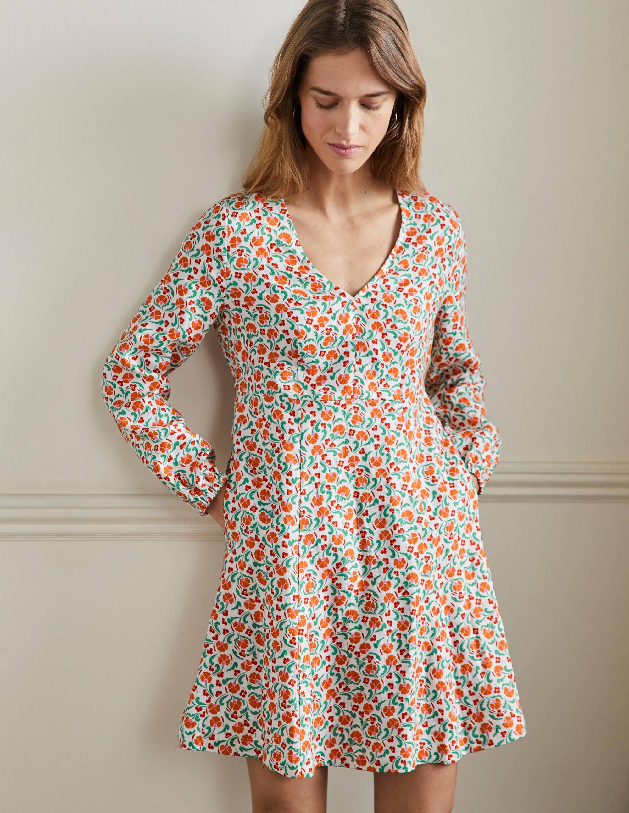 A woman wearing a bright papaya V-neck mini dress with a delicate floral pattern, long sleeves, and a floaty skirt.