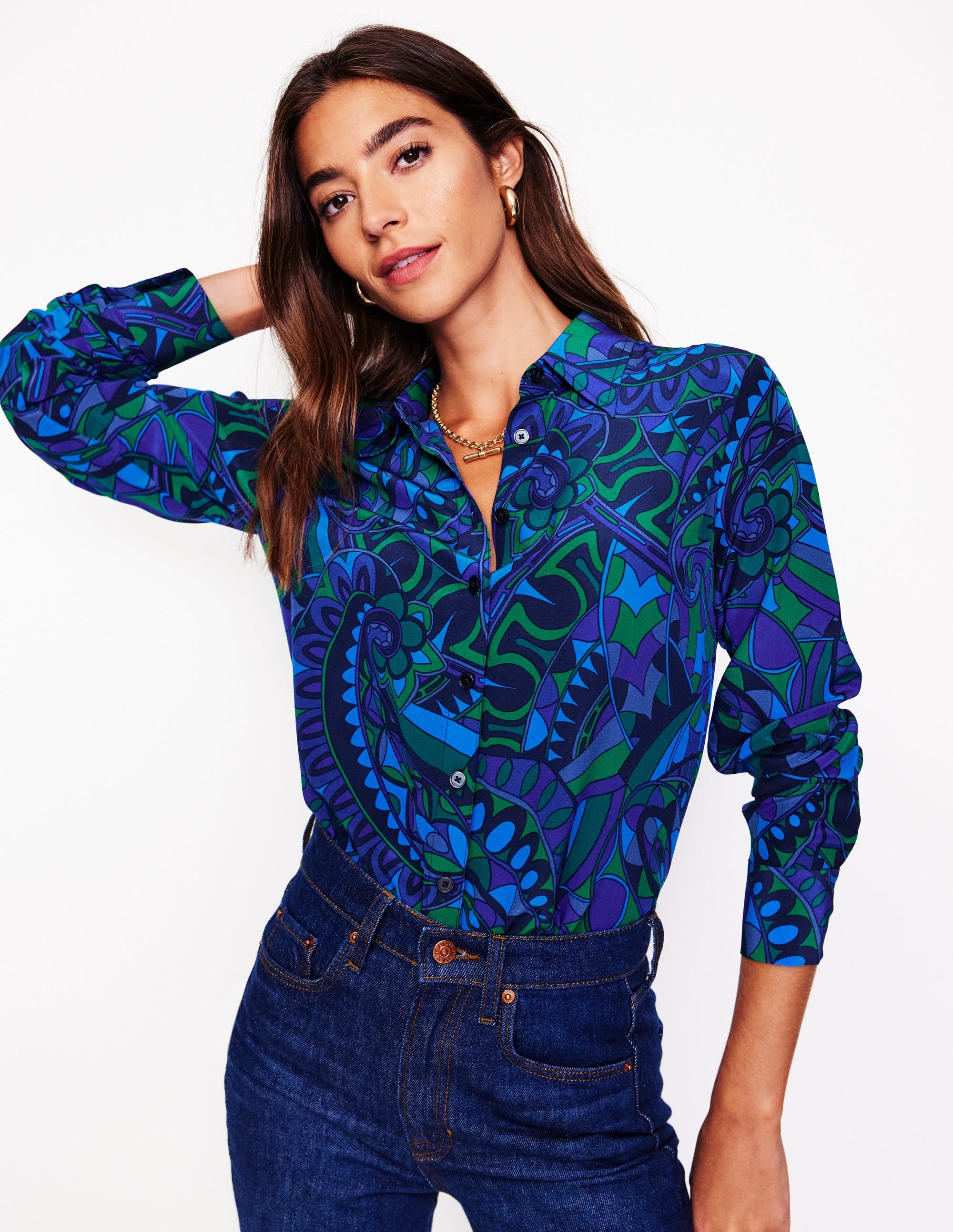 A woman wearing a long-sleeved silk shirt with a colorful paisley print in shades of blue, green, and purple, with a classic collar and button-down front.
