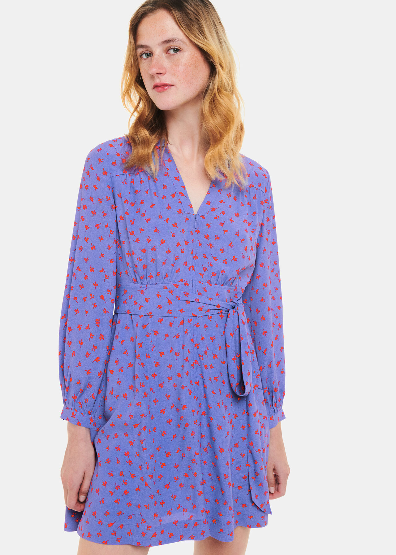 A woman wearing a purple dress with red petal motifs, V-neck, collar, waist belt, and long sleeves.