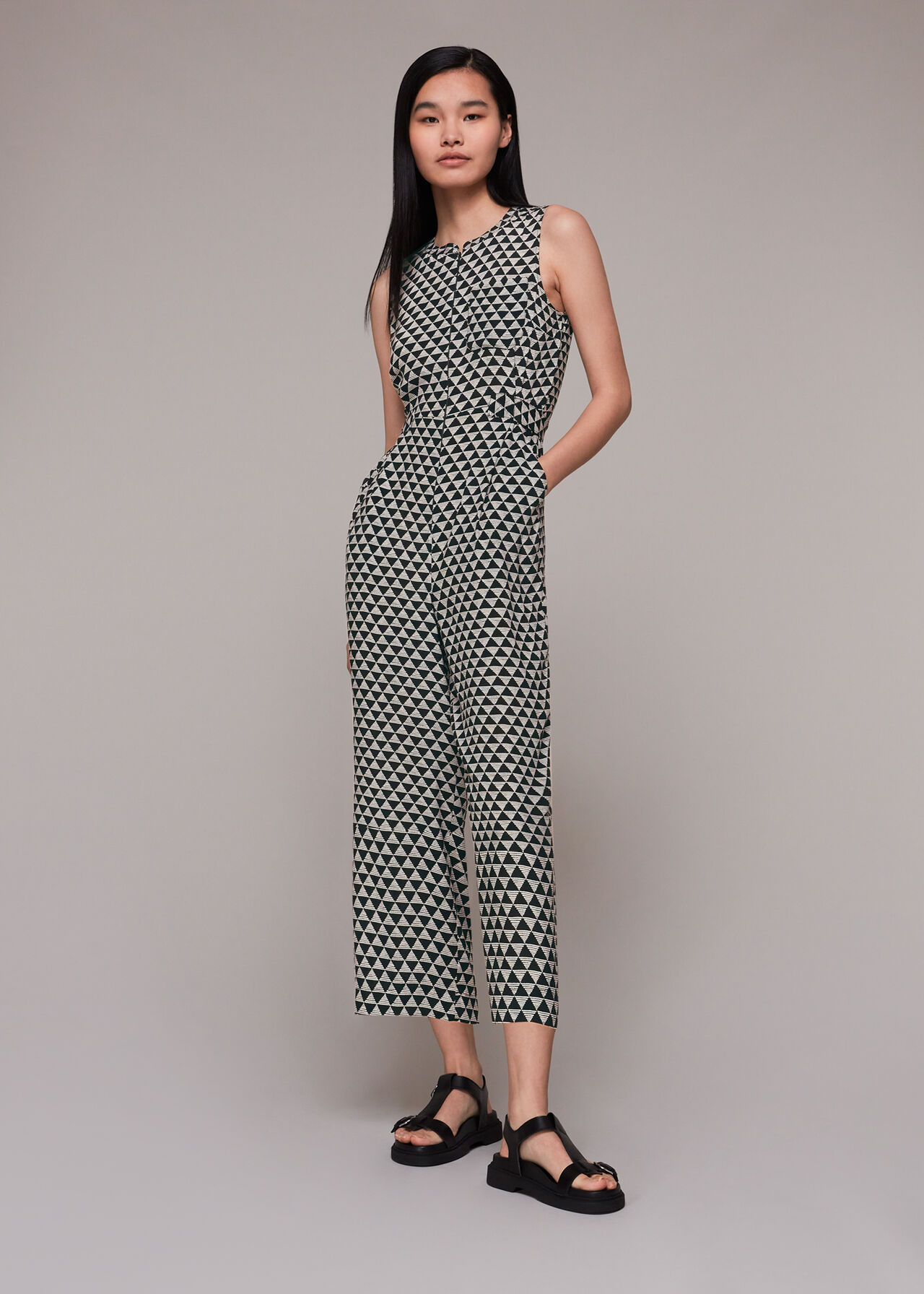 A woman wearing a black and white triangle checkerboard jumpsuit with a round neck and centre front zip, relaxed fit through the leg.