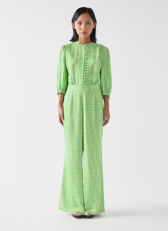 A woman wearing a green swirl print jumpsuit with long sleeves, frilled neck and cuffs, and wide-leg trousers.