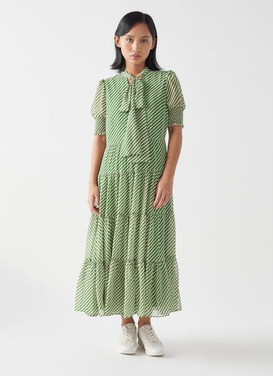 A woman wearing a green and white striped tie-neck georgette dress with smocked sleeves and a tiered skirt.