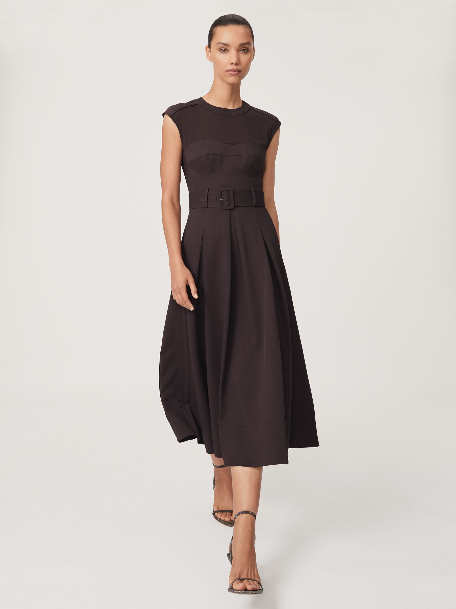 A woman wearing a burgundy sleeveless midi dress with mesh panels, a belt, and a pleated skirt.